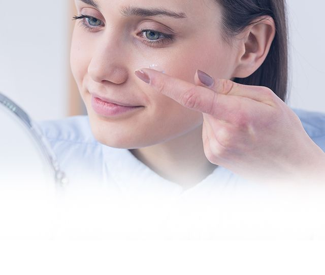 A young woman places a contact lens into her left eye.