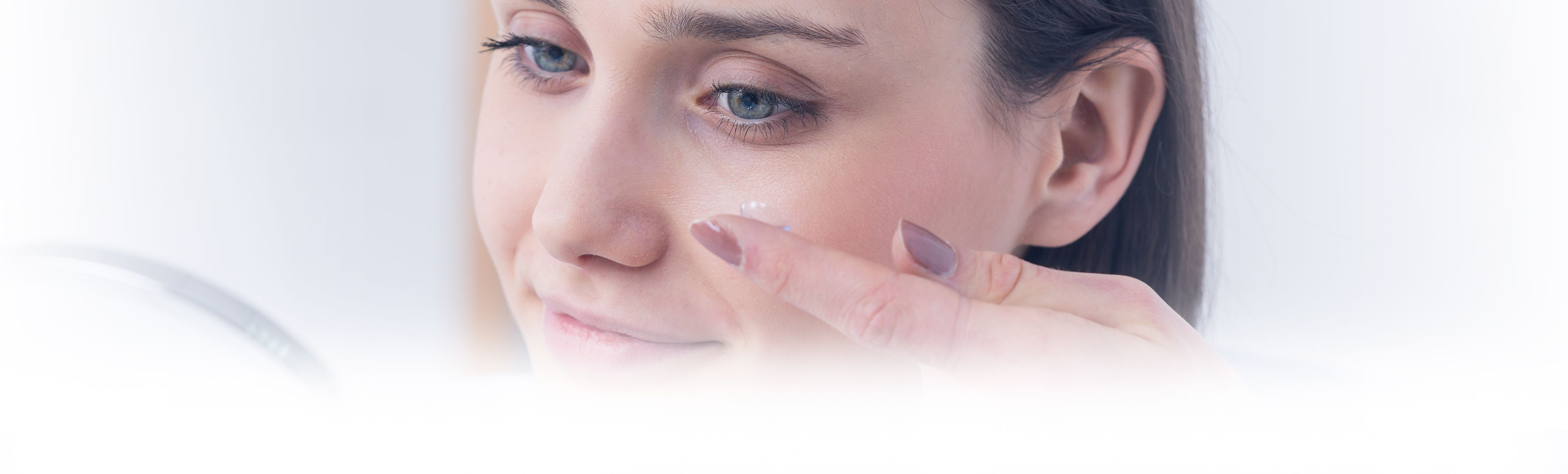 A young woman places a contact lens into her left eye.